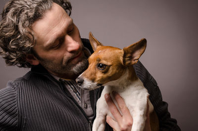 Mature man carrying jack russell terrier against gray background