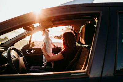 Woman sitting in car with dog during sunset
