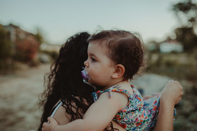 Side view of mother carrying cute daughter against sky