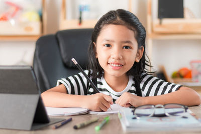 Portrait of girl writing on book at table