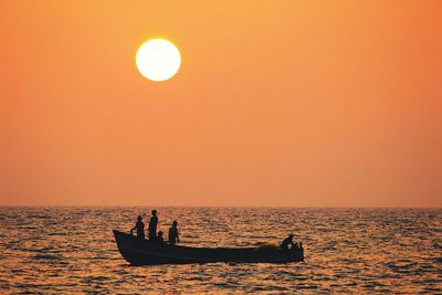 Silhouette people on boat in sea against orange sky during sunset