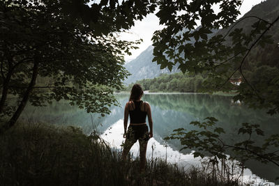 Rear view of man standing by lake in forest