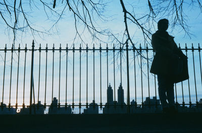 Rear view of silhouette man standing by railing against sky