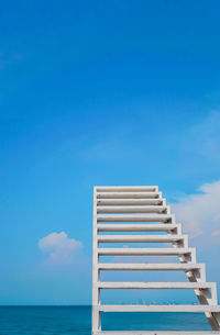 Low angle view of ladder by sea against blue sky