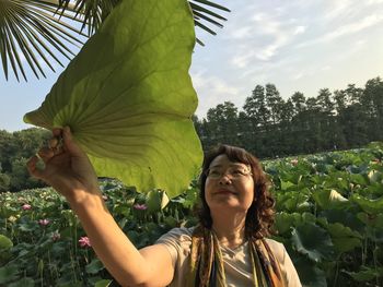 Portrait of young woman with leaves against sky