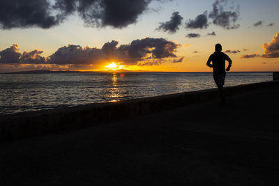 Silhouette man standing on beach against sky during sunset