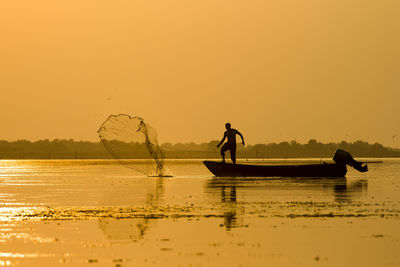 Silhouette fisherman fishing in lake against clear orange sky