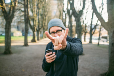 Portrait of mid adult man showing rock sign in park