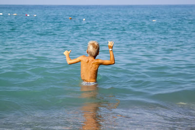 Rear view of shirtless boy standing in sea