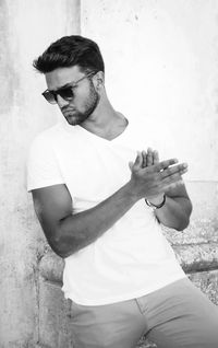 Young man wearing sunglasses looking away while standing against wall