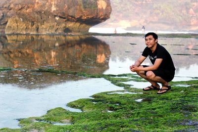 Portrait of man sitting on rock by lake