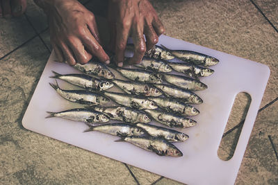 High angle view of cropped hand arranging fish on cutting board