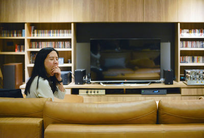 Woman yawning while sitting on sofa in living room at home