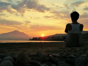 Rear view of women standing at beach against sky during sunset