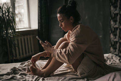 Woman using mobile phone while sitting on bed