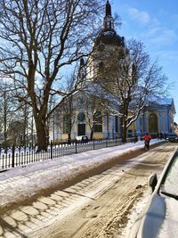 Road by bare trees and buildings against sky