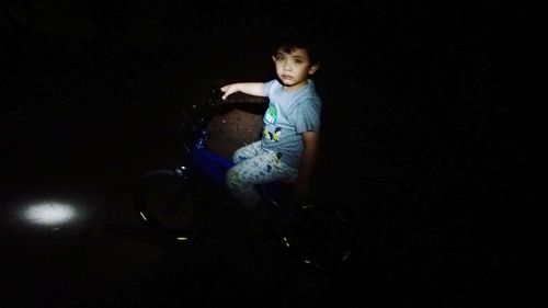 Side view of boy sitting against black background