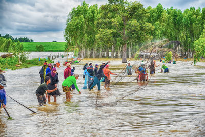 People at riverbank against sky