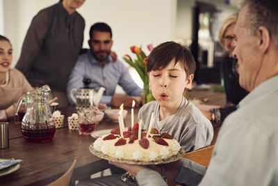 Boy blowing candles on birthday cake while enjoying in party with family at home