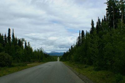 Road amidst field in mountains against sky