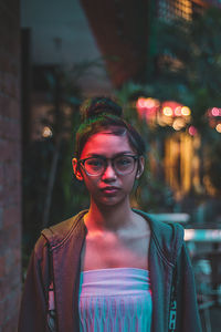 Portrait of young woman standing against illuminated wall at night