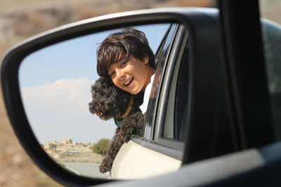 Reflection of smiling boy with dog in side-view mirror of car