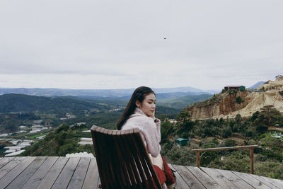 Portrait of young woman sitting on railing against mountain