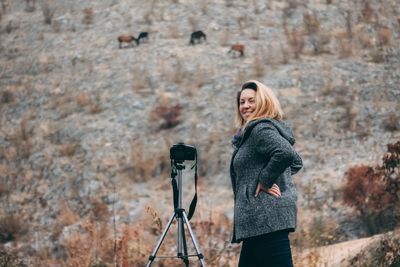 Portrait of young woman photographing horses while standing on field