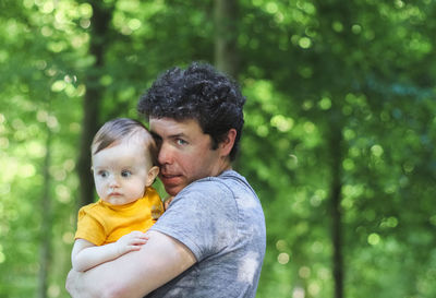 Caucasian young dad in a blue t-shirt gently hugs his little daughter in a yellow bodysuit