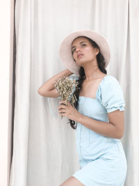 Portrait of beautiful young woman standing against curtain