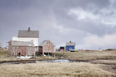 Old houses on field against cloudy sky