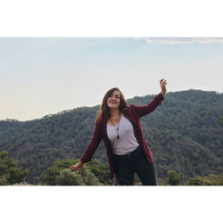 Portrait of smiling young woman standing on mountain against clear sky