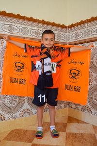 Full length portrait of smiling standing against orange wall