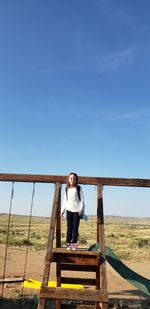 Woman standing on railing against blue sky