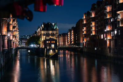 Illuminated bridge over river amidst buildings in city at night