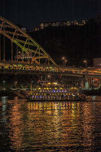 Illuminated bridge over river against sky at night