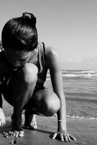 Full length of wet girl crouching at sandy beach