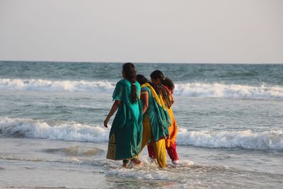 Women in traditional clothes walking at beach against clear sky