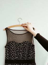 Close-up of hand holding dress on coathanger against white background