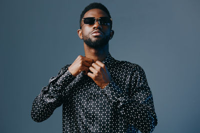 Portrait of young man wearing sunglasses against gray background