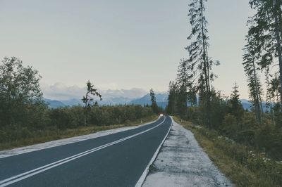 Empty road by trees against sky