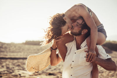 Man kissing woman while carrying her on shoulders at beach