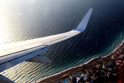 Airplane wing flying above greek town - coast