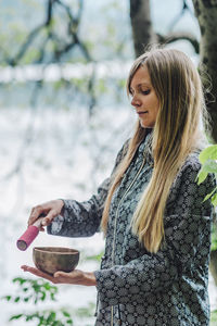 Side view of young woman holding bowl while standing in park
