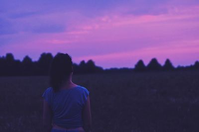 Rear view of boy standing on field against sky during sunset