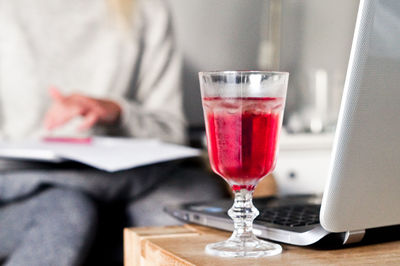 Close-up of red drink in glass by laptop on table 