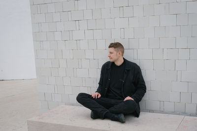 Portrait of young man sitting against wall