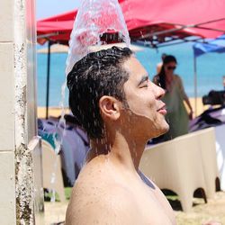 Water falling on shirtless man during sunny day