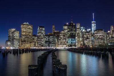 Illuminated modern buildings by river against sky at night