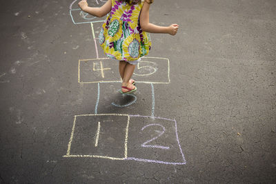 Low section of girl playing hopscotch on road